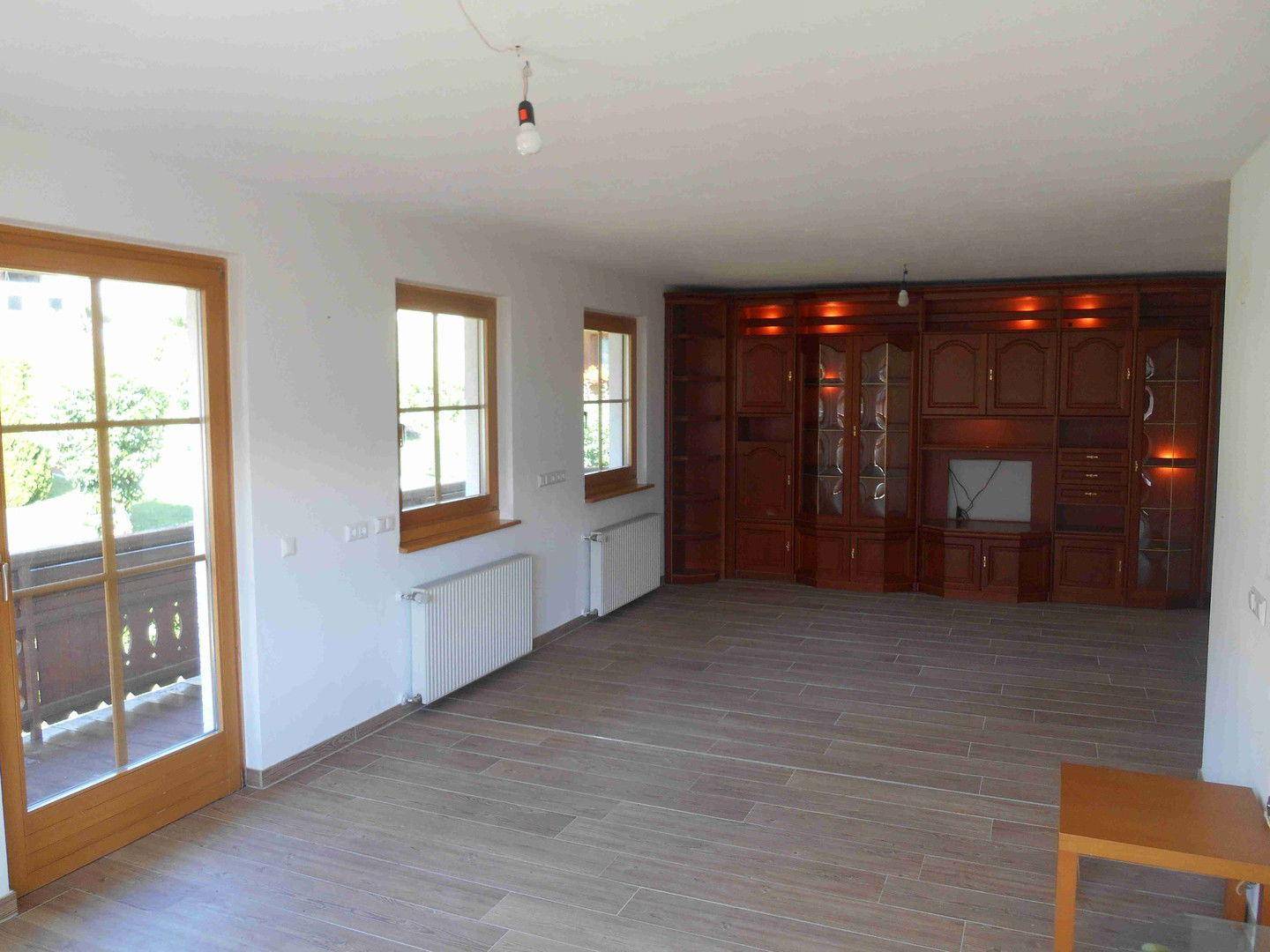 Geräumiges Wohnzimmer mit Fliesenboden, Zugang zum Balkon und einer großen Holzschrankwand.
