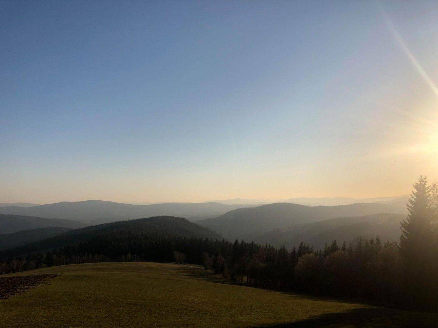Weitläufige Berglandschaft bei Sonnenuntergang mit grünen Wiesen und bewaldeten Hügeln.
