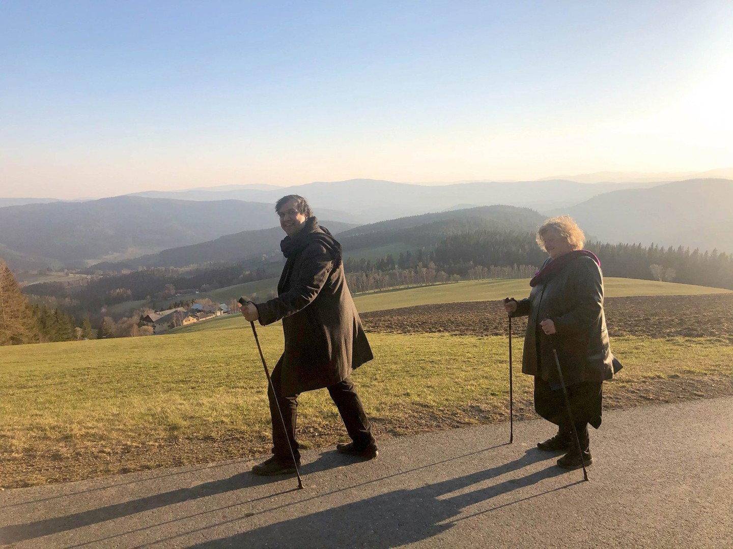 Zwei Personen beim Nordic Walking auf einem Weg mit weitem Blick über die hügelige Landschaft.