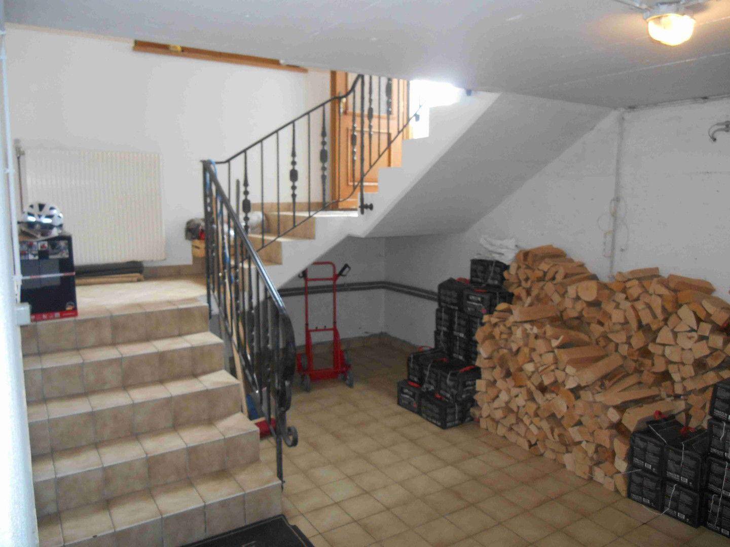 Kellerbereich mit gefliestem Boden, Holzstapel und Treppenzugang zum Obergeschoss.