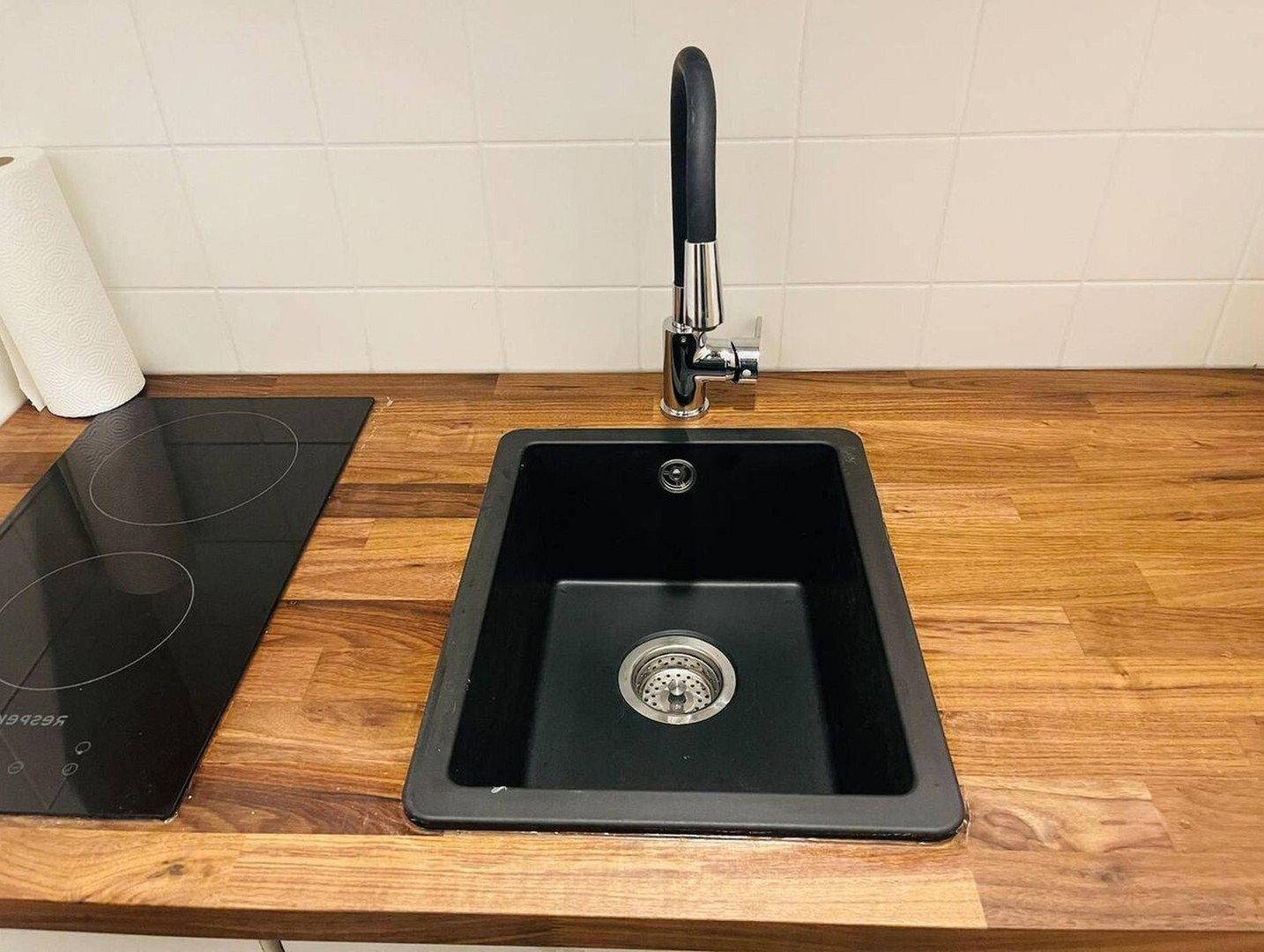 Schwarzes Spülbecken und Induktionskochfeld in einer Küche mit Holzarbeitsplatte und weißem Fliesenspiegel.