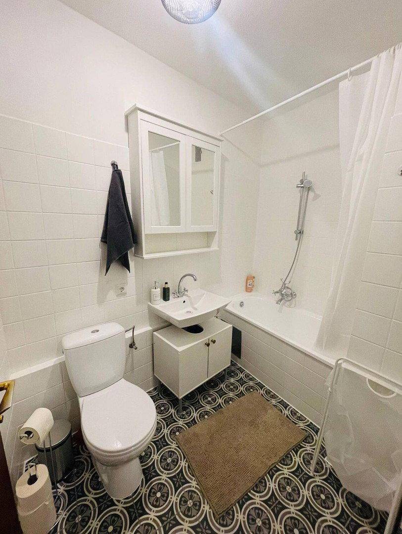Helles Badezimmer mit Badewanne, Toilette, Waschbecken und gemustertem Fliesenboden.