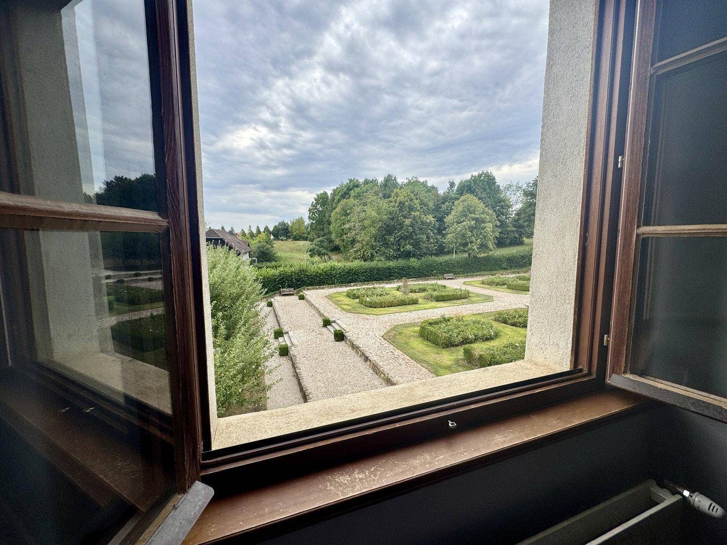 Blick aus dem Fenster auf einen gepflegten formalen Garten mit Kieswegen und grünen Hecken.