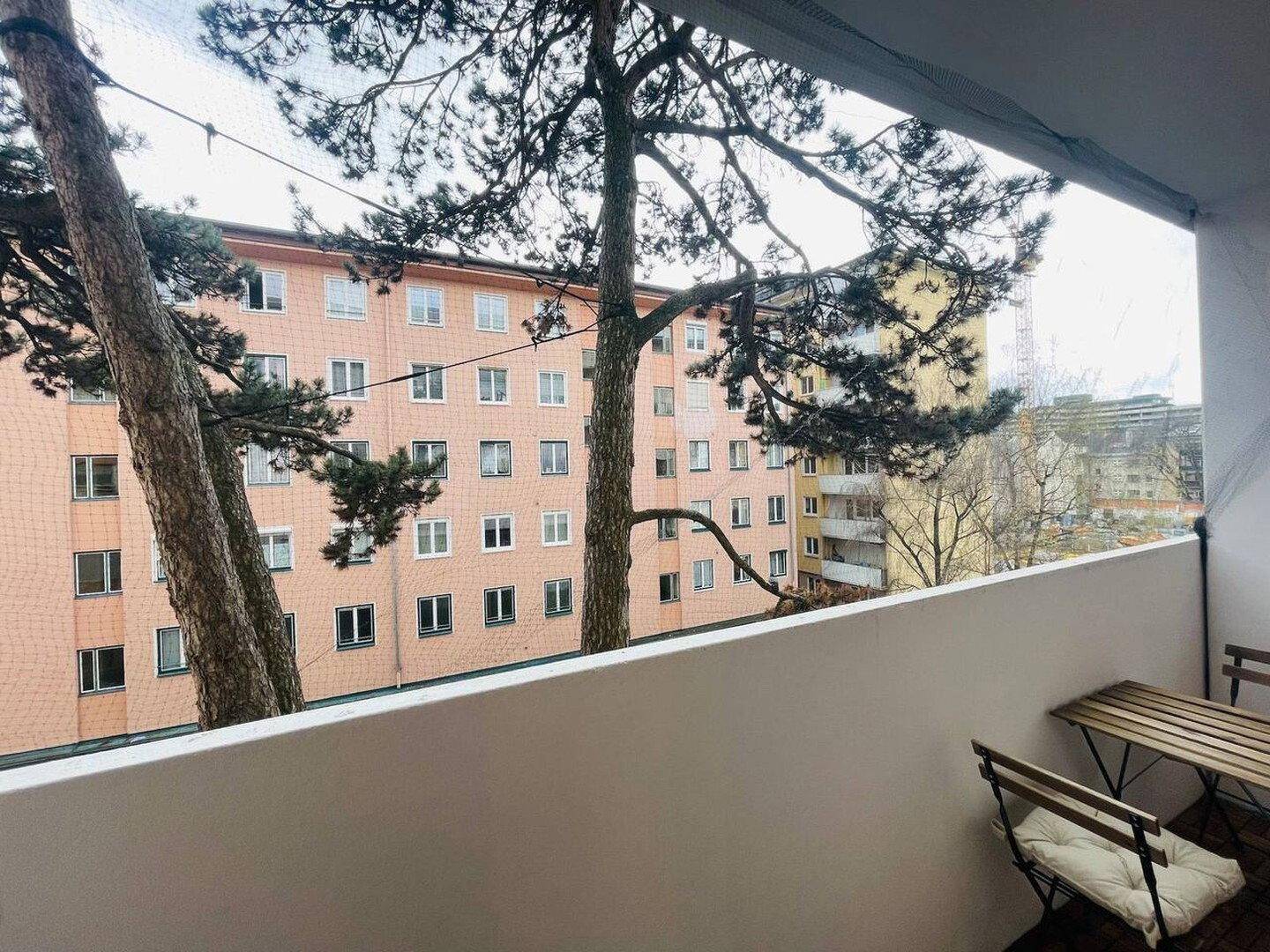 Balkon mit Holzboden und Blick auf umliegende Wohngebäude und Bäume.