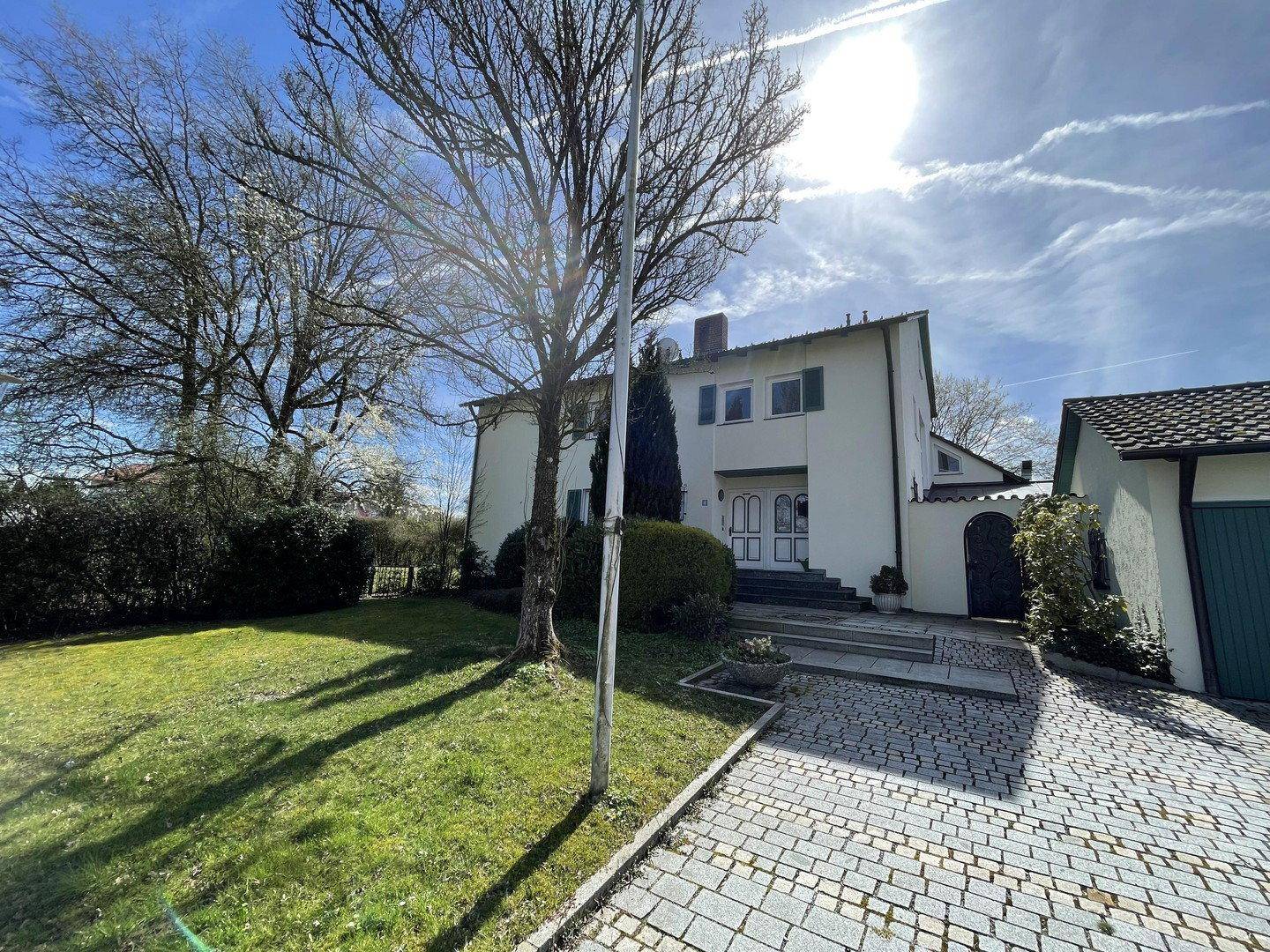 Vorderansicht des Hauses mit gepflasterter Auffahrt, Vorgarten und sonnigem Wetter.