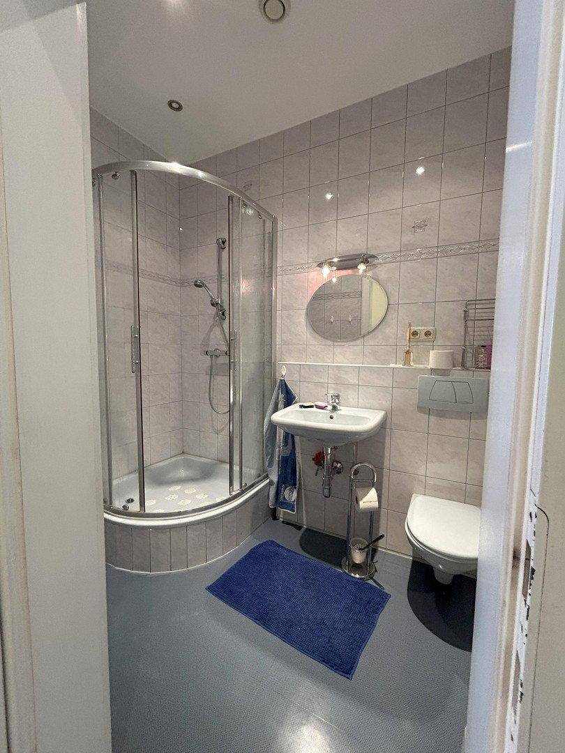 Modernes Badezimmer mit Duschkabine, Waschbecken, WC und hellen Fliesen an den Wänden.