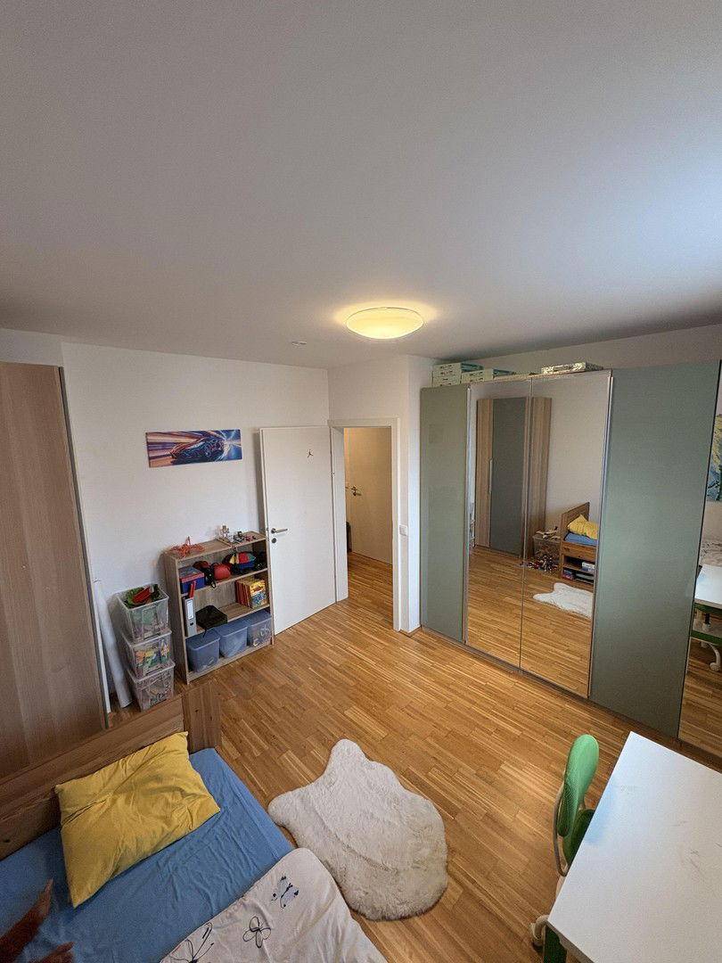 Geräumiges Kinderzimmer mit Parkettboden, großem Kleiderschrank und viel Tageslicht.