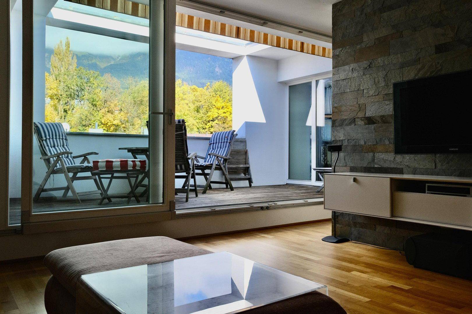 Gemütliches Wohnzimmer mit bequemer Couch, Holzboden und Zugang zu einer Terrasse mit Bergblick.