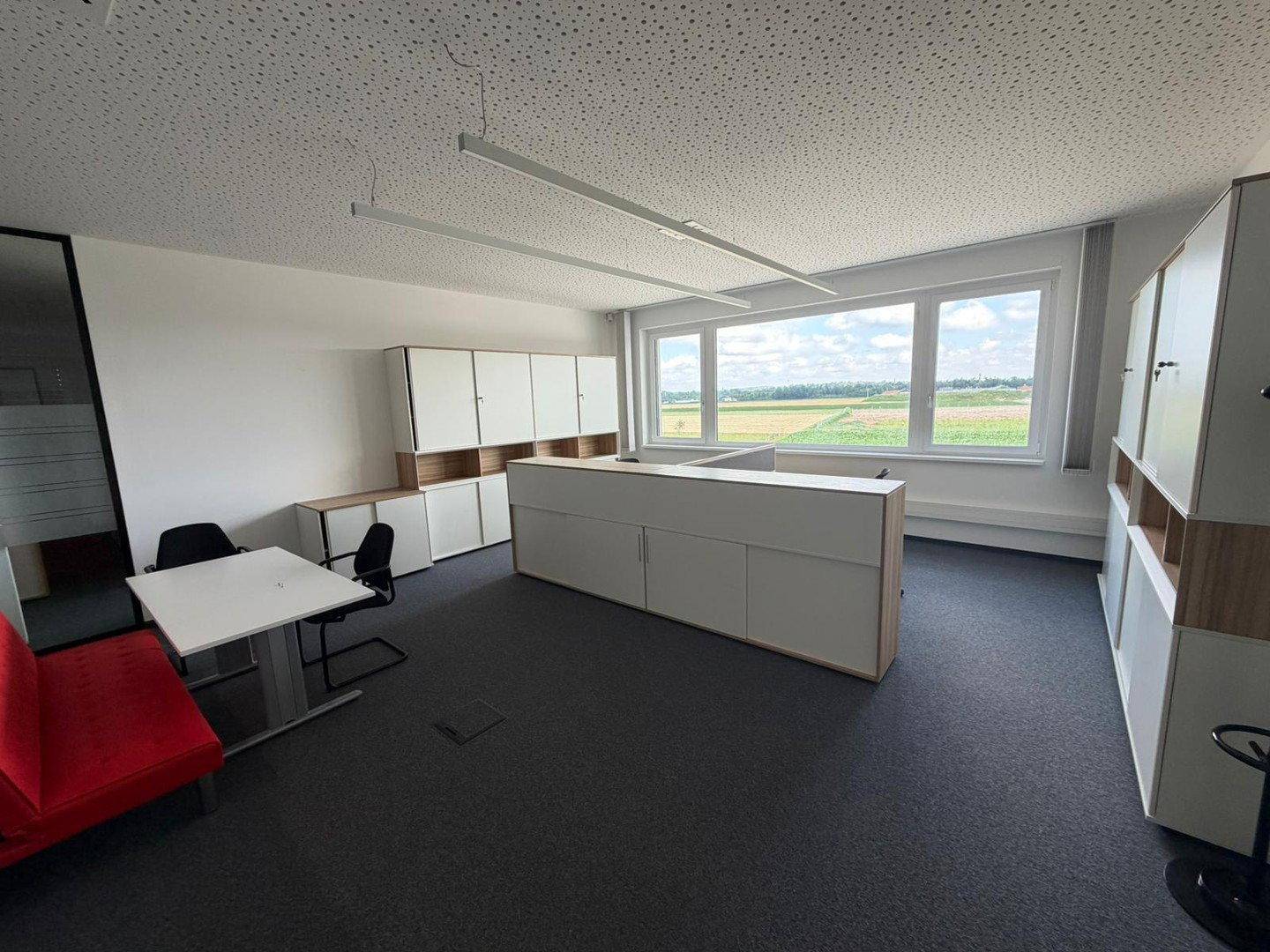 Geräumiges Büro mit mehreren Arbeitsbereichen, Stauraum und weitem Blick ins Grüne.