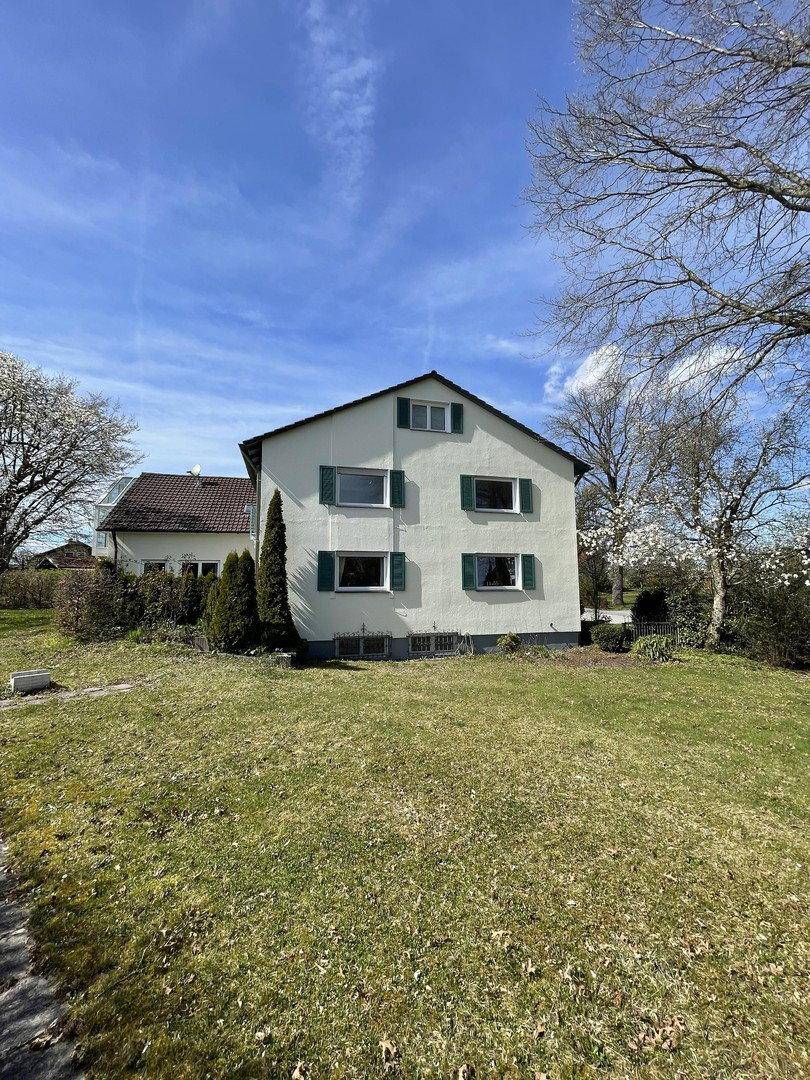 Rückansicht des Hauses mit großem Garten und grüner Umgebung unter blauem Himmel.