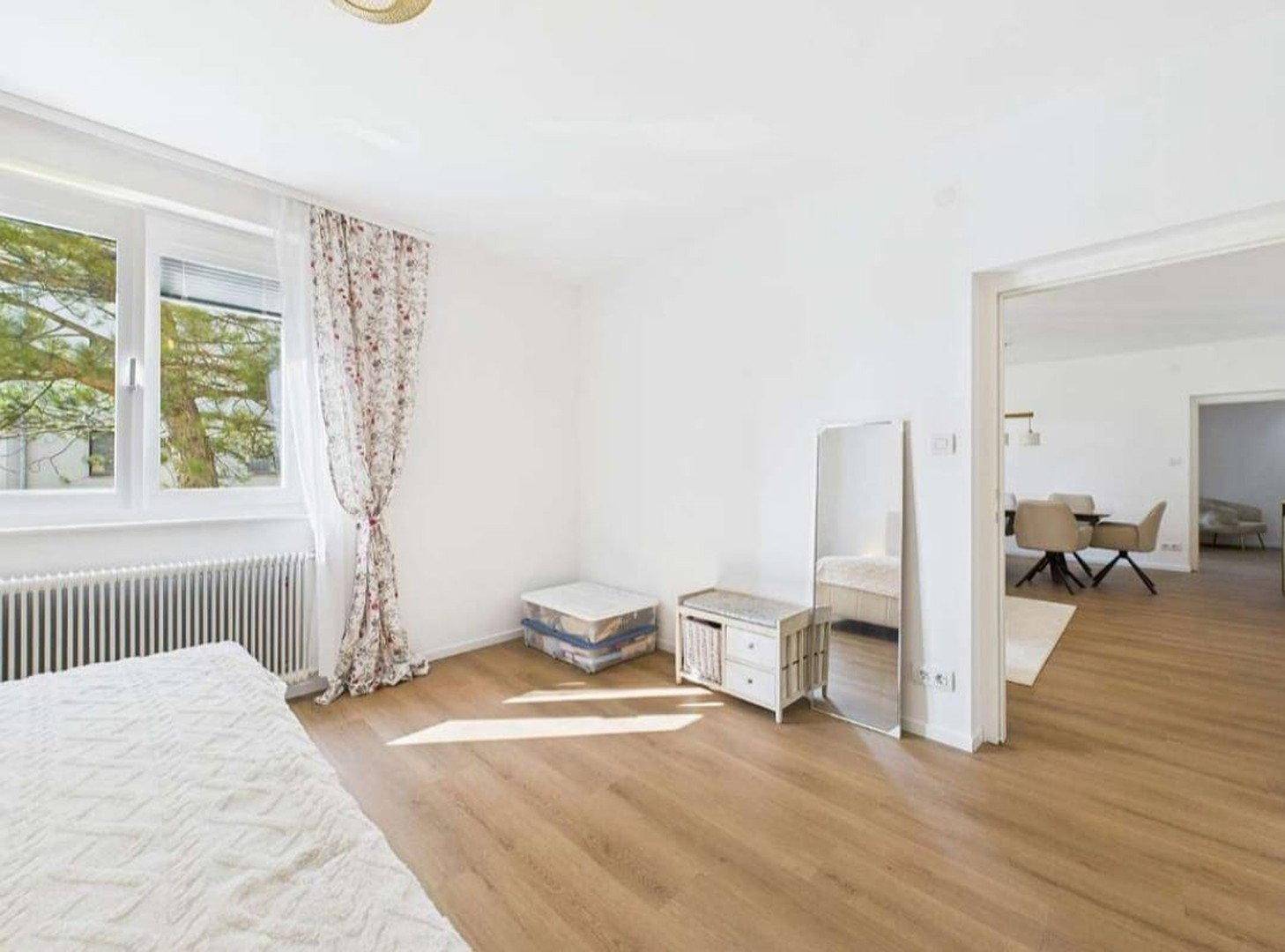Helles Schlafzimmer mit Parkettboden, großem Fenster und Blick ins Grüne.