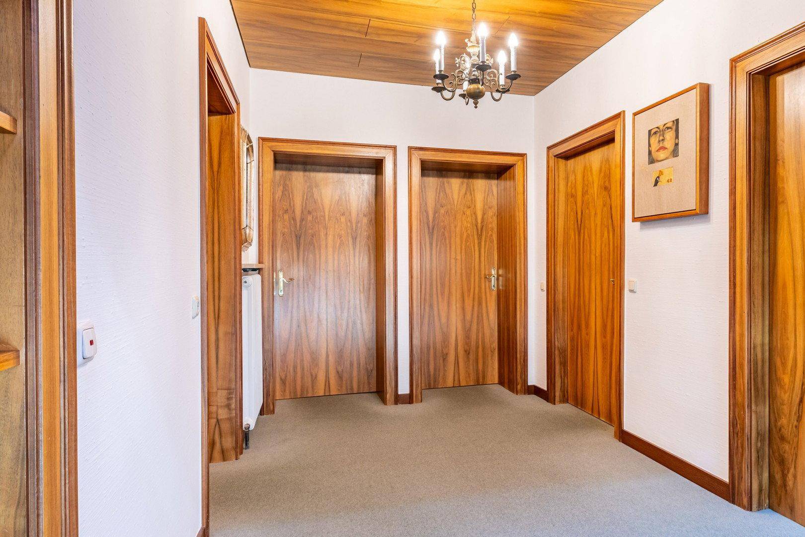 Geräumiger Flur mit mehreren Holztüren, Teppichboden und Deckenleuchte.
