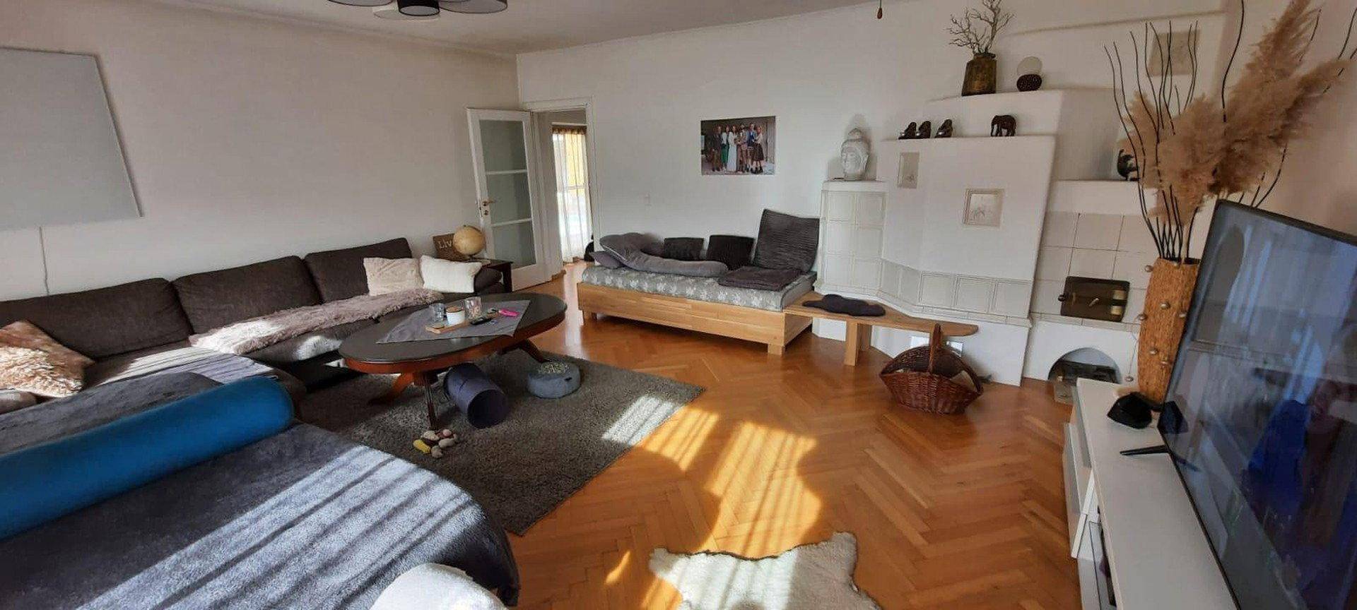 Gemütliches Wohnzimmer mit großem Sofa, Parkettboden und einem traditionellen Kachelofen für wohlige Wärme.