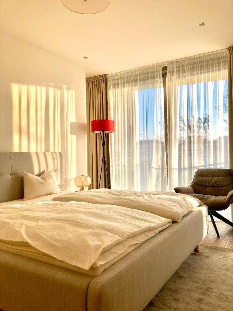 Helles Schlafzimmer mit großem Bett, bequemen Stühlen und großen Fenstern mit Vorhängen.