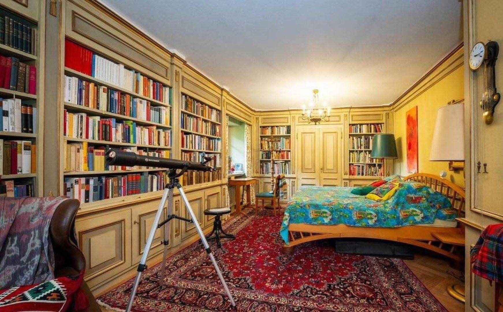 Schlafzimmer mit integrierten Bücherregalen, Holzboden und einem Teleskop für Sternenbeobachtung.