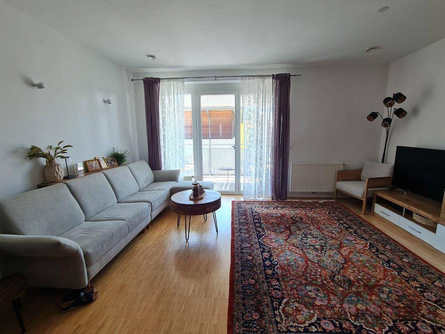 Geräumiges Wohnzimmer mit großem Sofa, Teppich und Zugang zum Balkon.