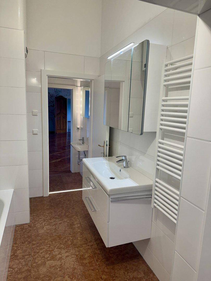 Modernes Badezimmer mit weißen Fliesen, Waschtisch und beheiztem Handtuchhalter.