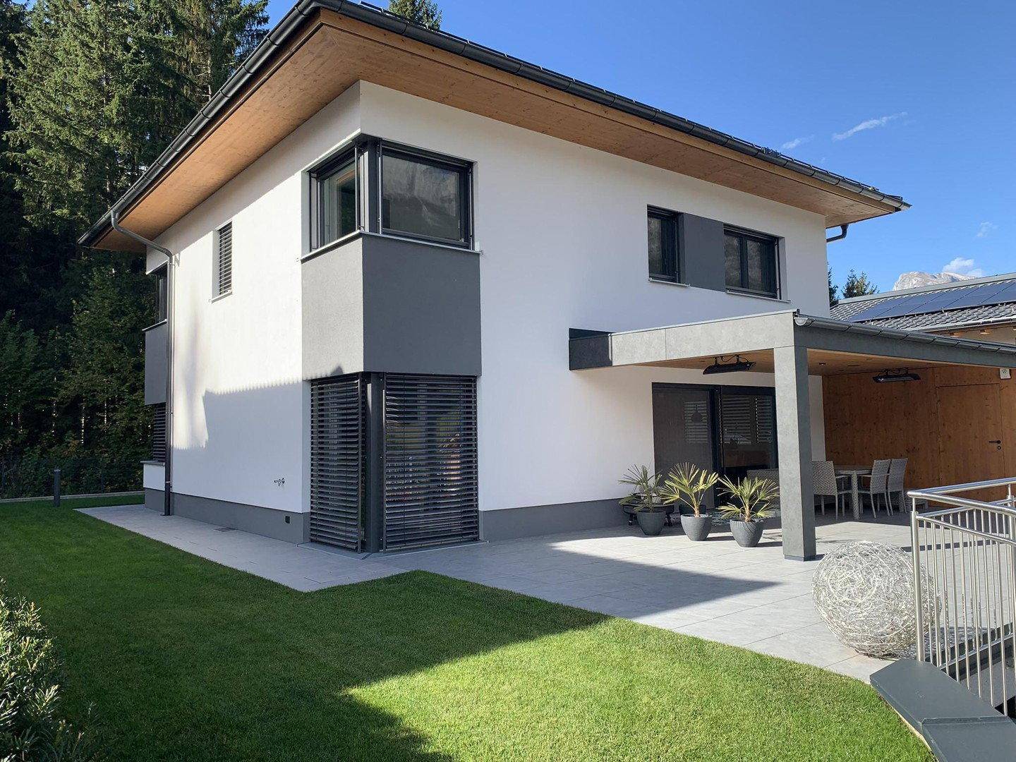 Modernes Einfamilienhaus mit weißer Fassade, großen Fenstern und überdachter Terrasse.