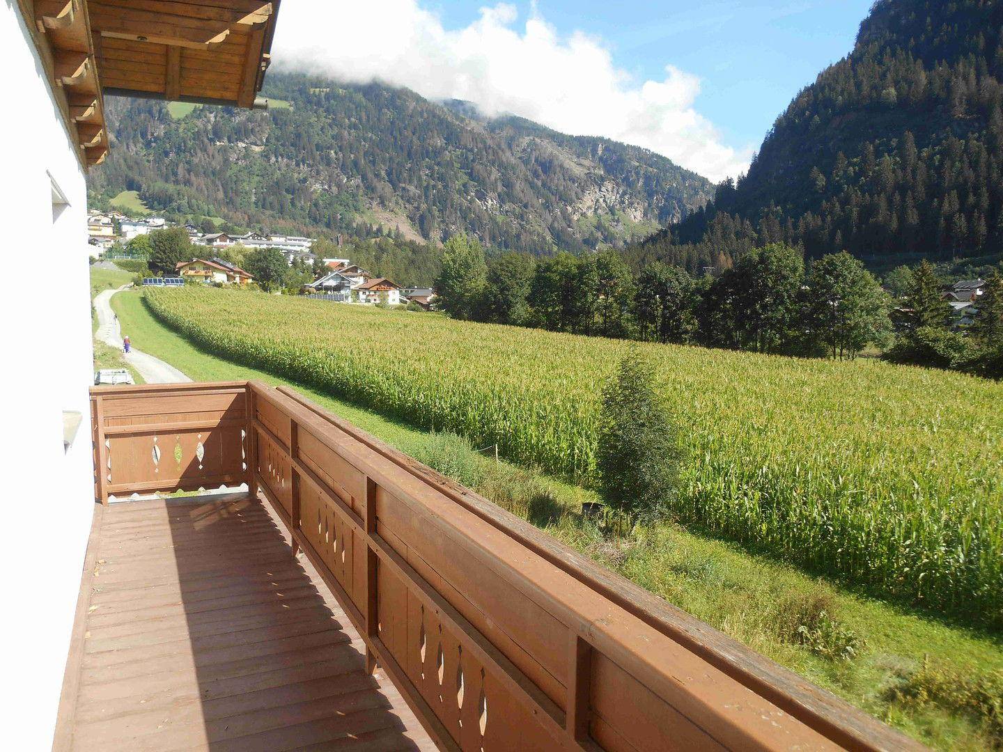 Geräumiger Holzbalkon mit weitem Blick über grüne Felder und die umliegende Berglandschaft.