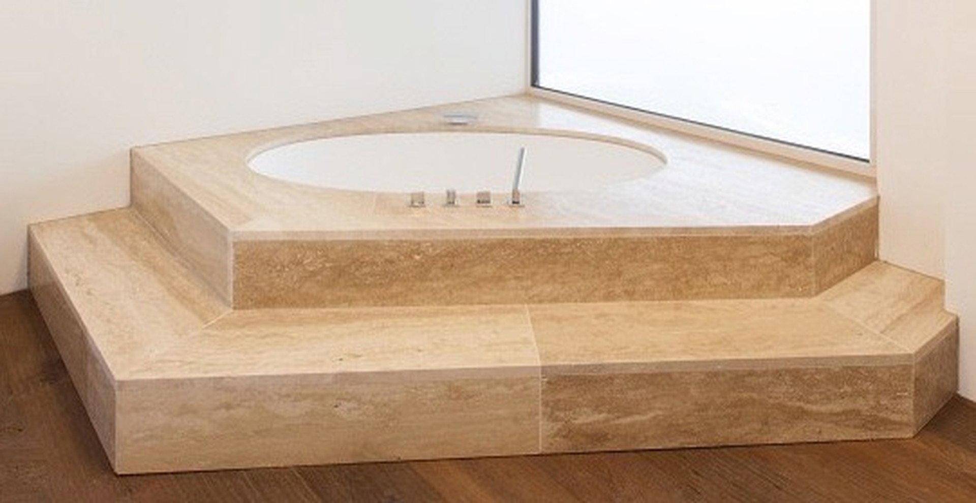 Elegante Eckbadewanne aus Naturstein, erhöht und in eine moderne Badezimmerlandschaft integriert.