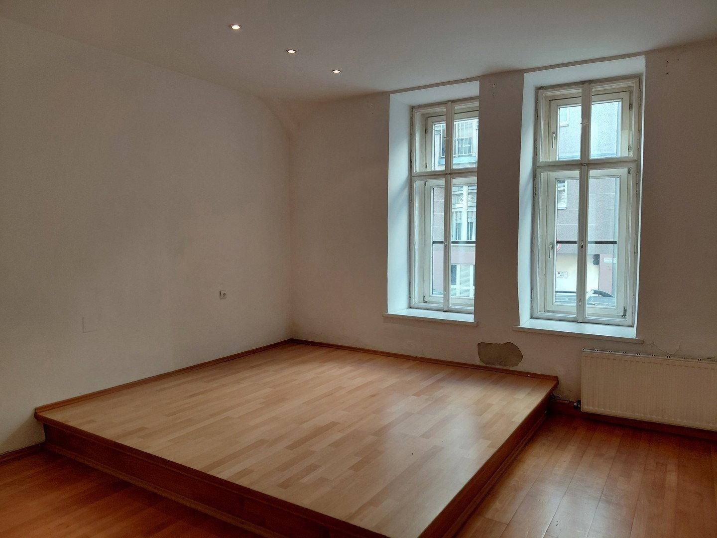 Schlafzimmer mit Holzboden, erhöhter Schlafplattform und zwei Fenstern.