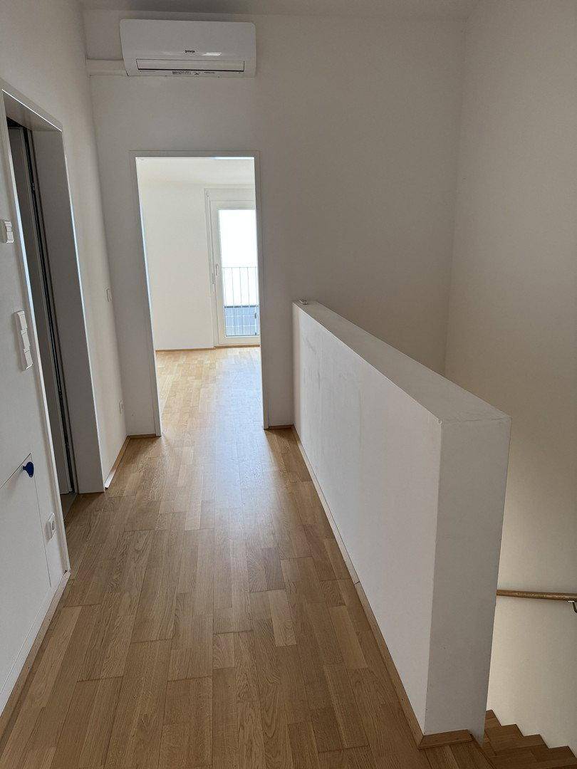 Heller Flur mit Holzfußboden und Klimaanlage, der zu einem Zimmer mit französischem Balkon führt.