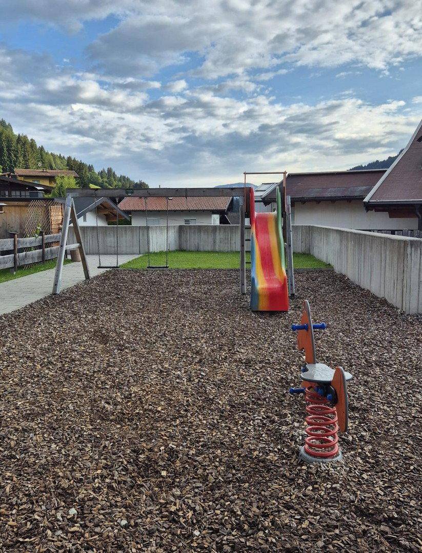 Kinderspielplatz mit Rutsche und Schaukeln auf Rindenmulchboden.