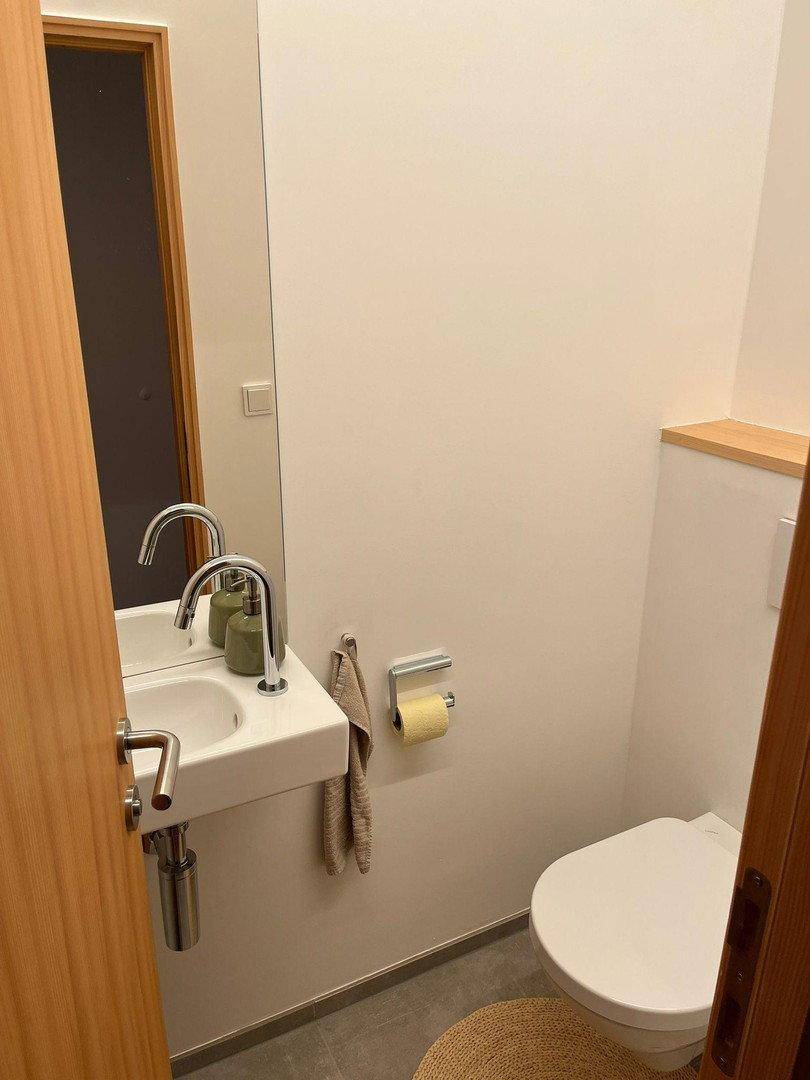 Kleines Gäste-WC mit wandmontierter Toilette, Einzelwaschbecken und einem großen Spiegel.