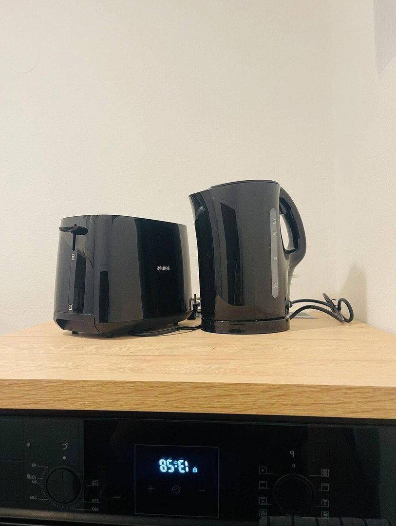 Schwarzer Toaster und Wasserkocher auf einer hellen Holzarbeitsplatte über einem Backofen.