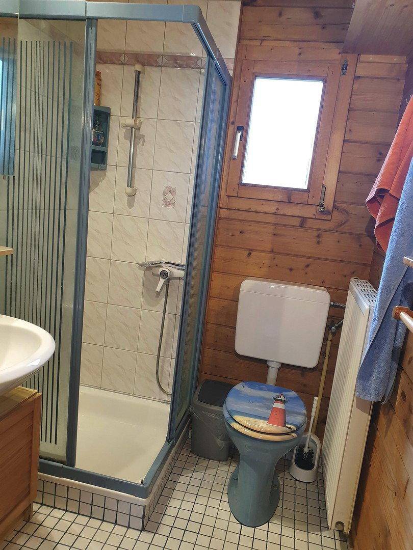 Badezimmer mit Duschkabine, WC und Holzvertäfelung an den Wänden sowie Fenster.