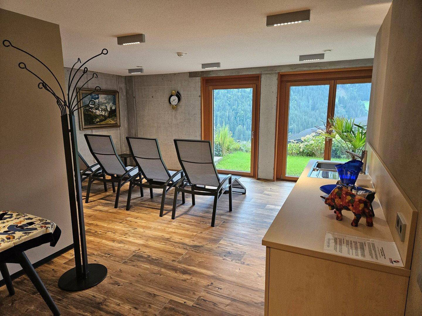 Entspannungsbereich mit Liegestühlen, Holzboden und großen Fenstern mit Blick ins Grüne.