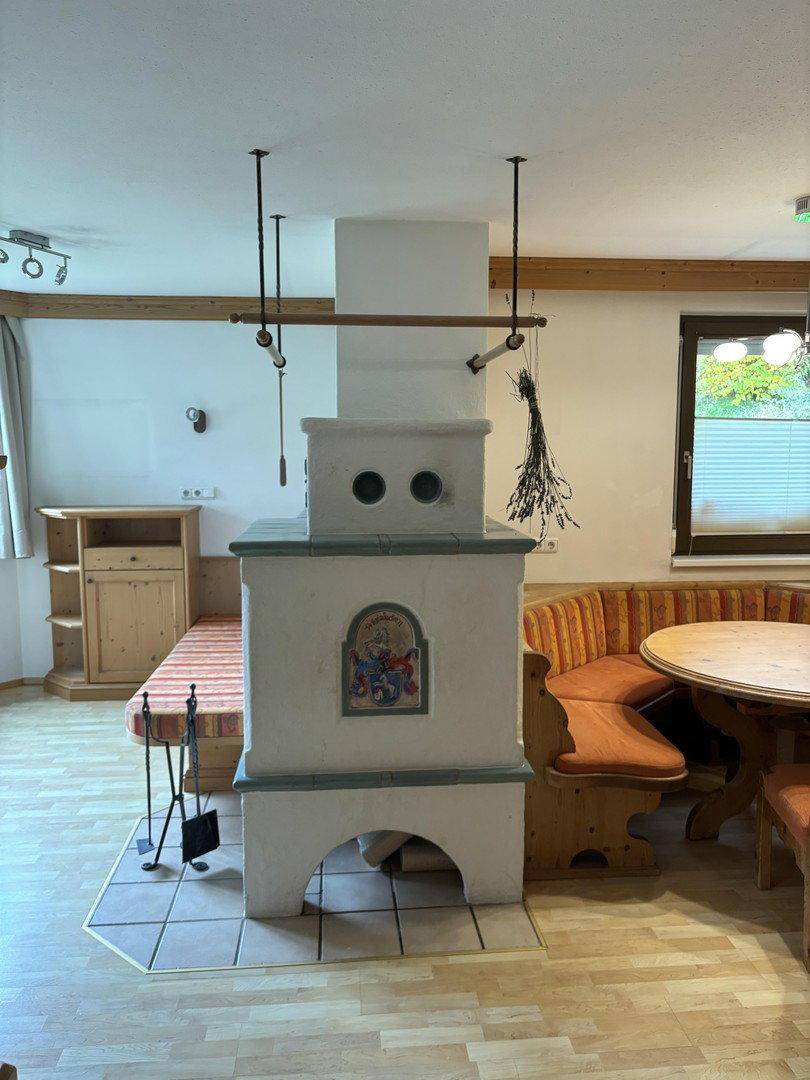 Traditioneller Wohn-Essbereich mit einem Kachelofen, einer Eckbank und einem Holztisch.