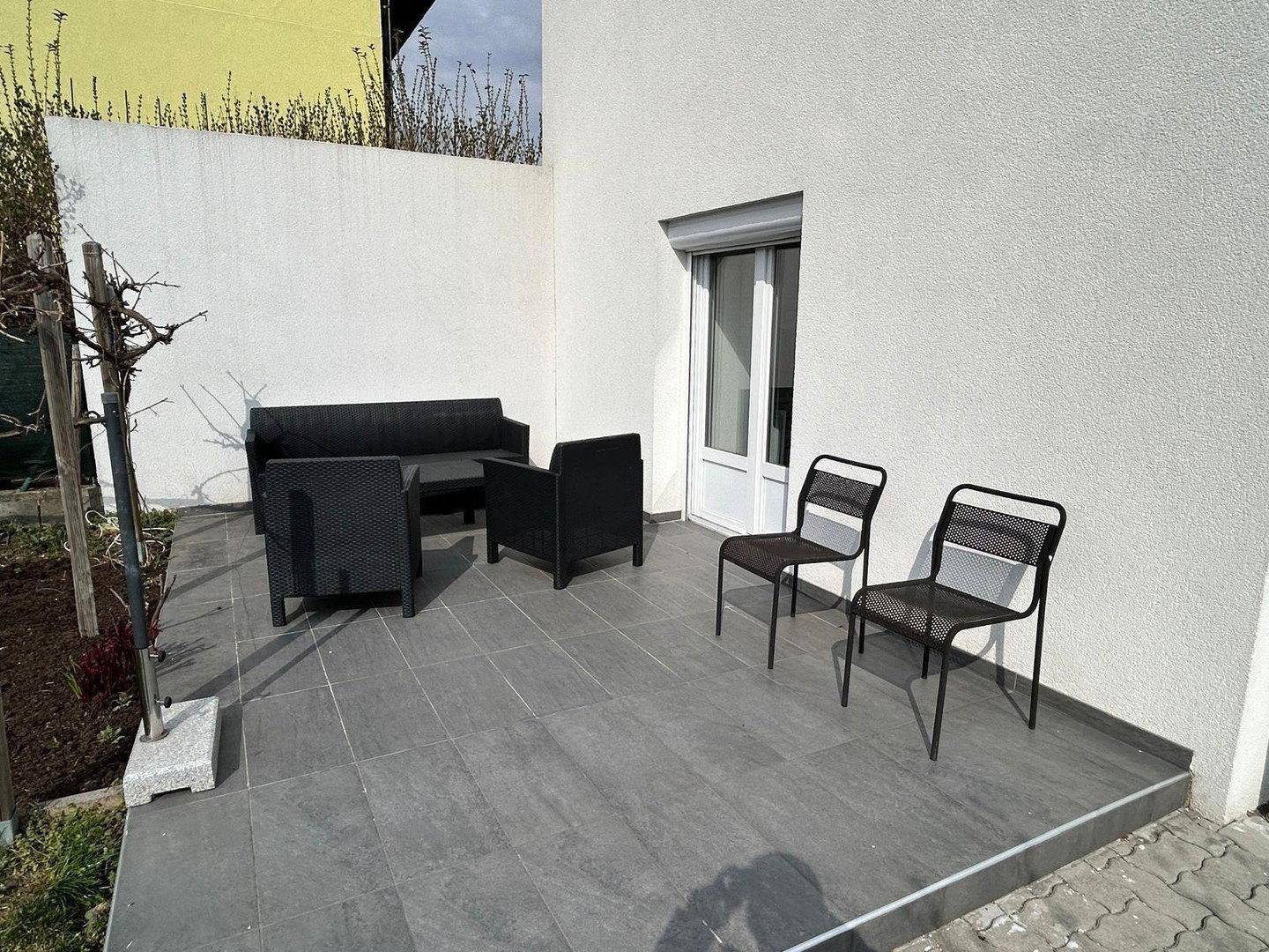 Moderne Terrasse mit grauen Fliesen und bequemen Outdoor-Sitzmöbeln neben der Hauswand.