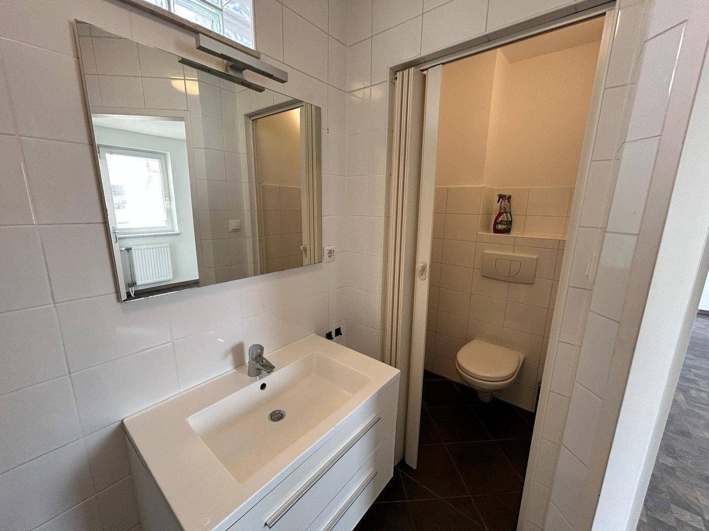 Badezimmer mit modernem Waschtisch, Spiegel und separatem WC-Bereich.