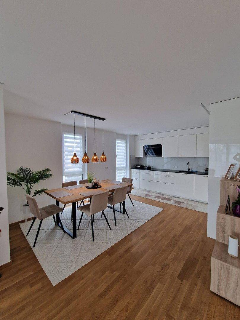 Moderne offene Küche mit weißen Hochglanzfronten und Essbereich auf Holzparkett.