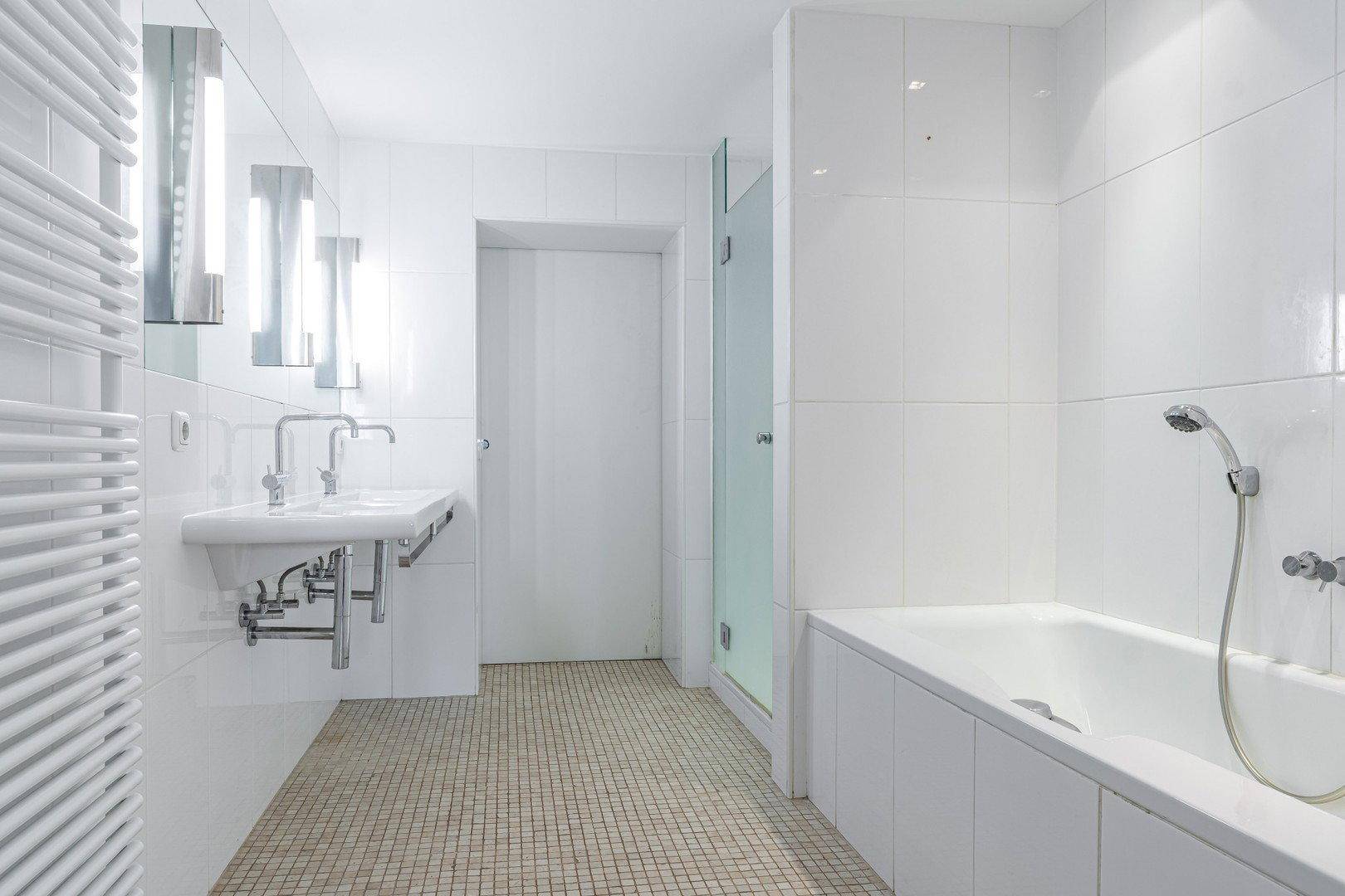Modernes Badezimmer in Weiß mit Badewanne, Doppelwaschbecken und Handtuchheizkörper.