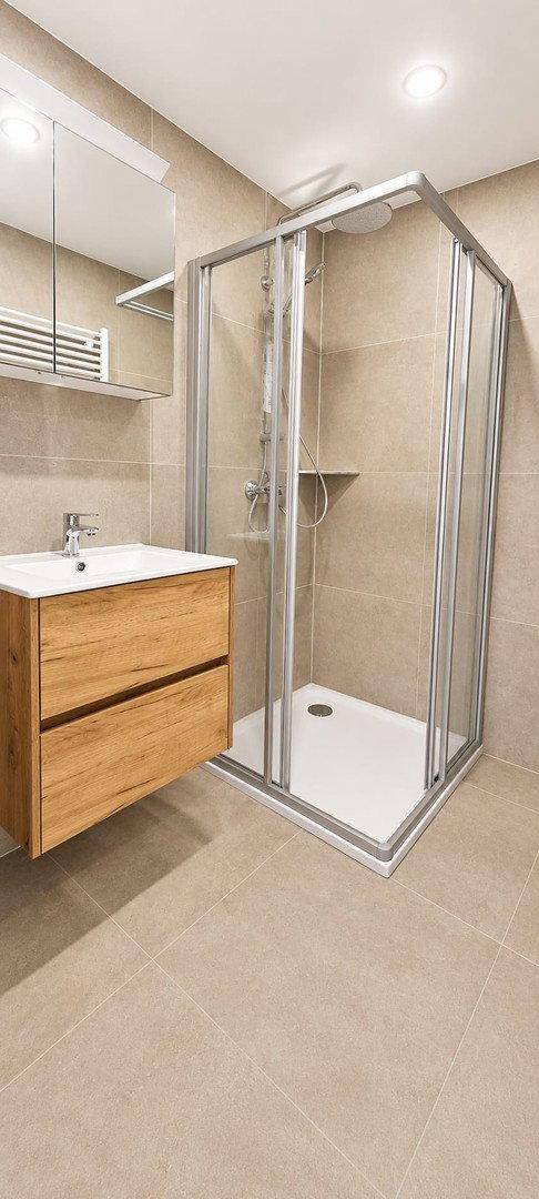 Modernes Badezimmer mit beigefarbenen Fliesen, Duschkabine und elegantem Holzwaschtisch.