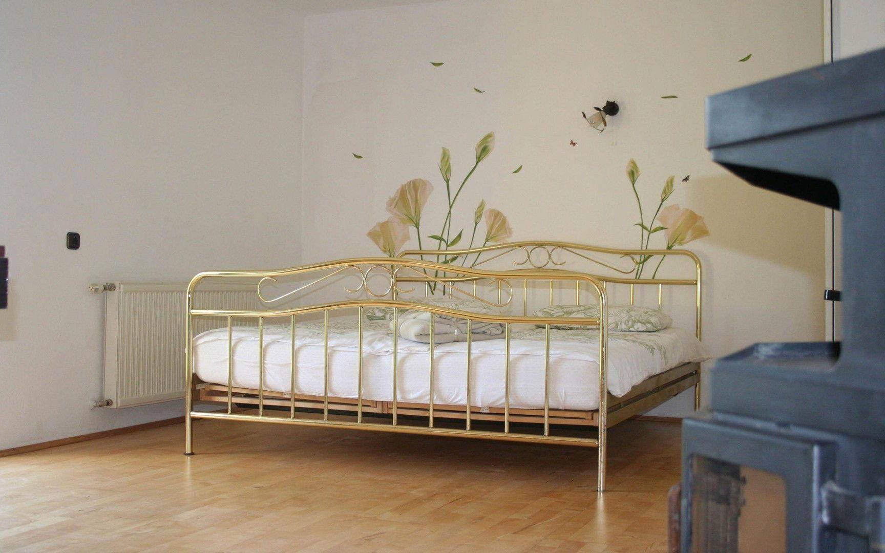 Gemütliches Schlafzimmer mit goldenem Metallbettgestell und floraler Wanddekoration.
