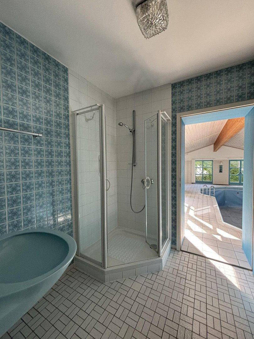 Badezimmer mit blauen Fliesen, Dusche und Zugang zum Innenpoolbereich.