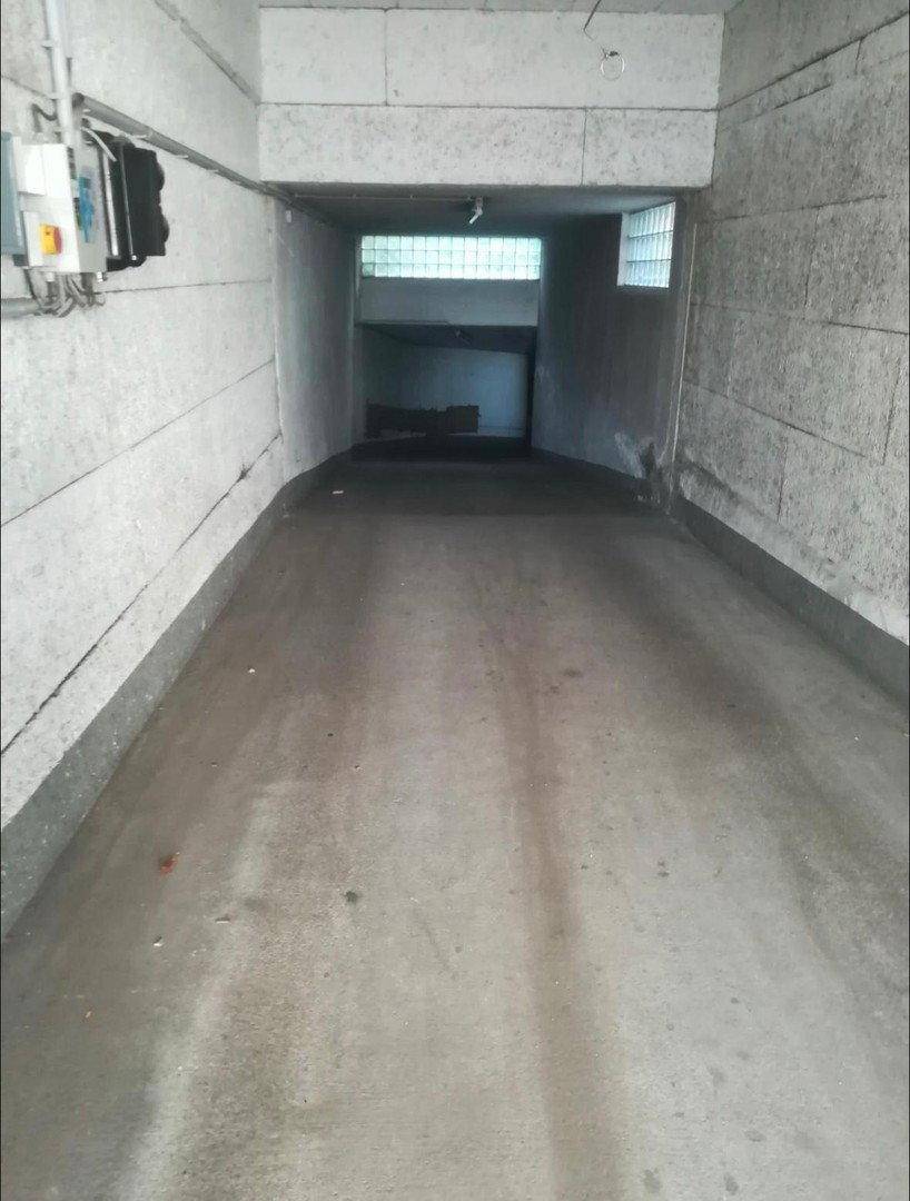 Langer, schmaler Betonweg in einer Tiefgarage oder einem Kellerbereich mit Glasbausteinen am Ende.