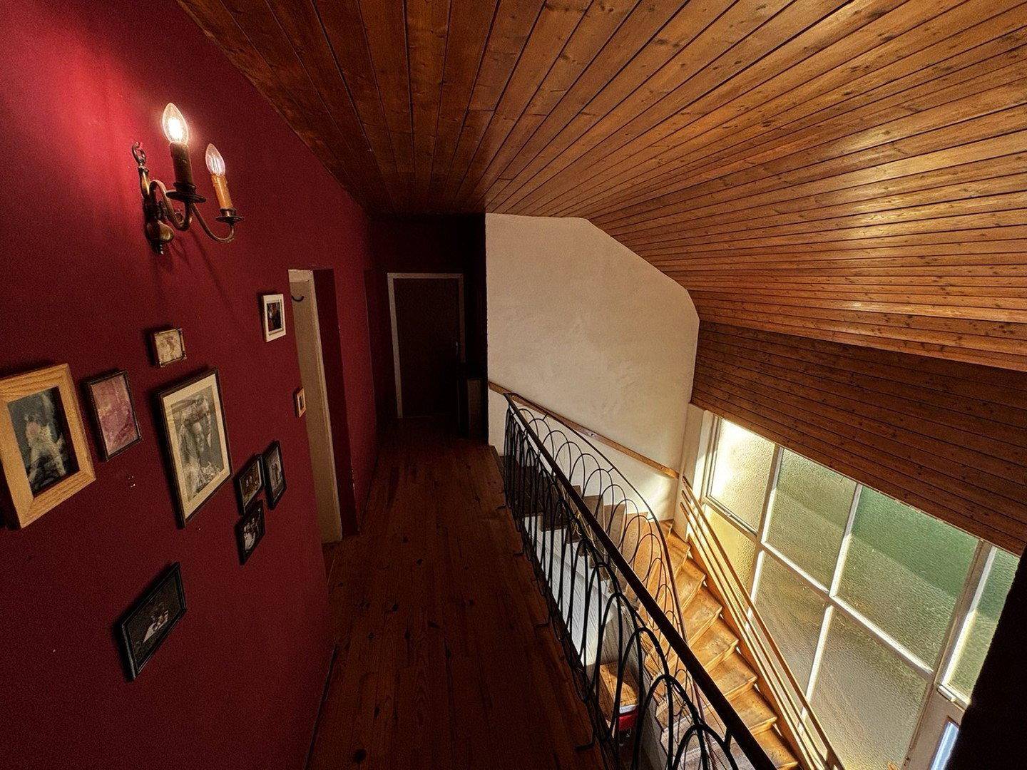 Oberer Flur mit Holzbalkendecke, roter Wand und Blick auf das Treppenhaus.