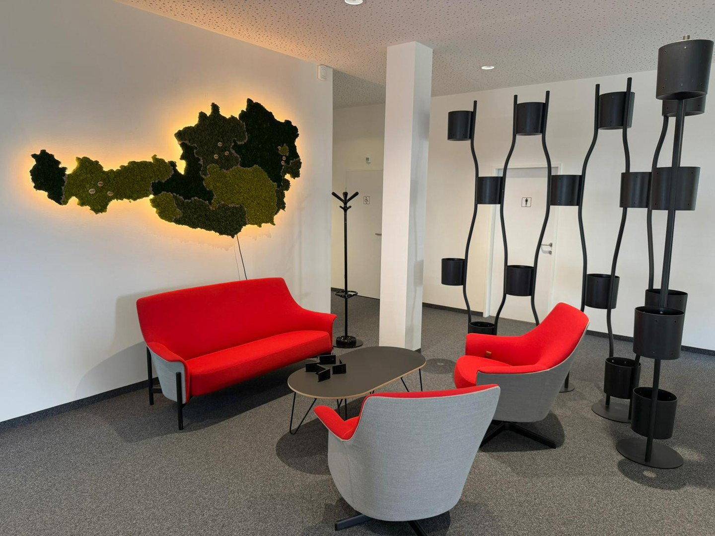 Gemütlicher Loungebereich mit roten Sofas, einem Couchtisch und einer beleuchteten Österreichkarte an der Wand.