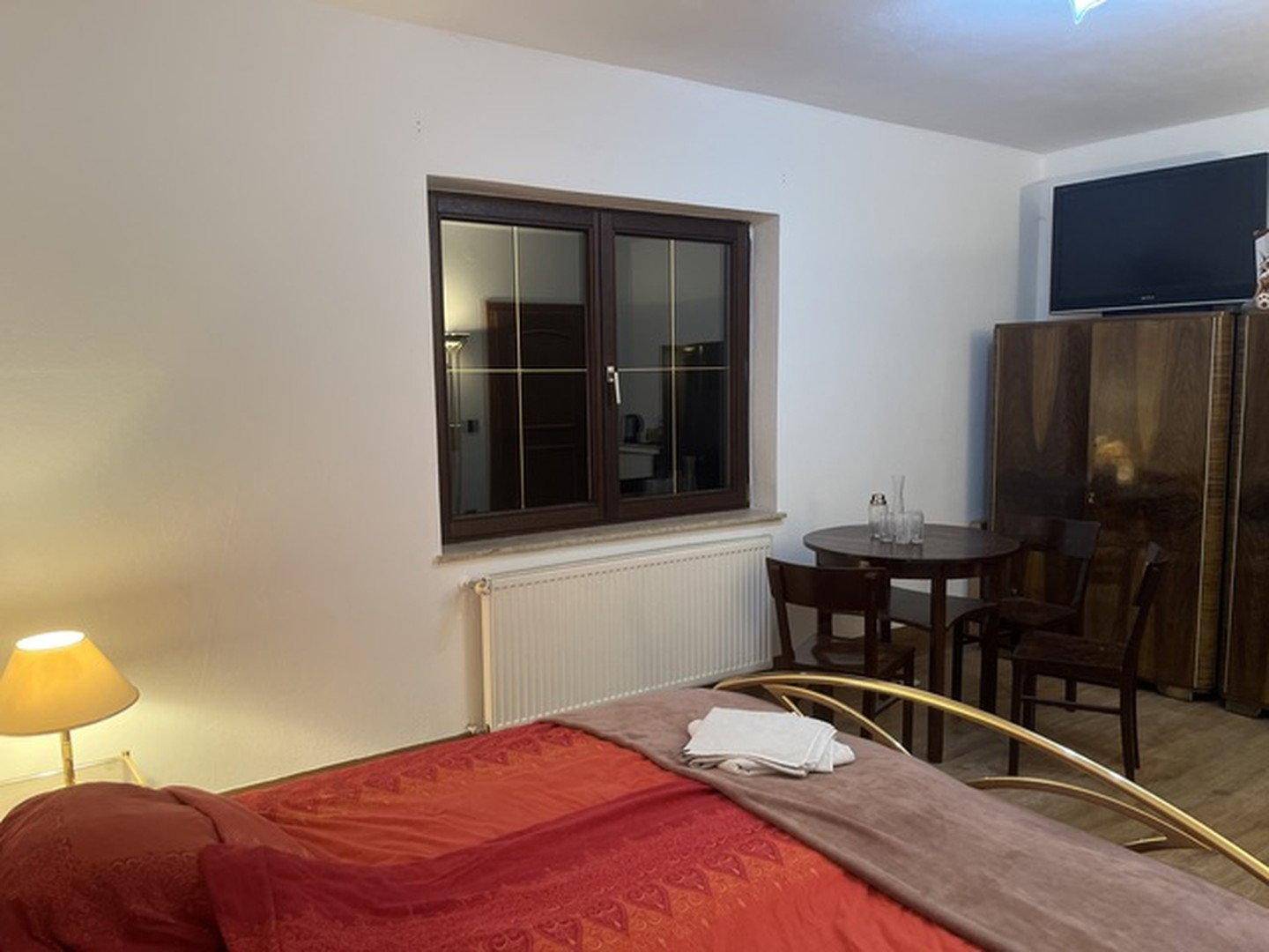 Schlafzimmer mit Doppelbett, Fenster, Heizkörper und klassischen Holzmöbeln in warmen Tönen.
