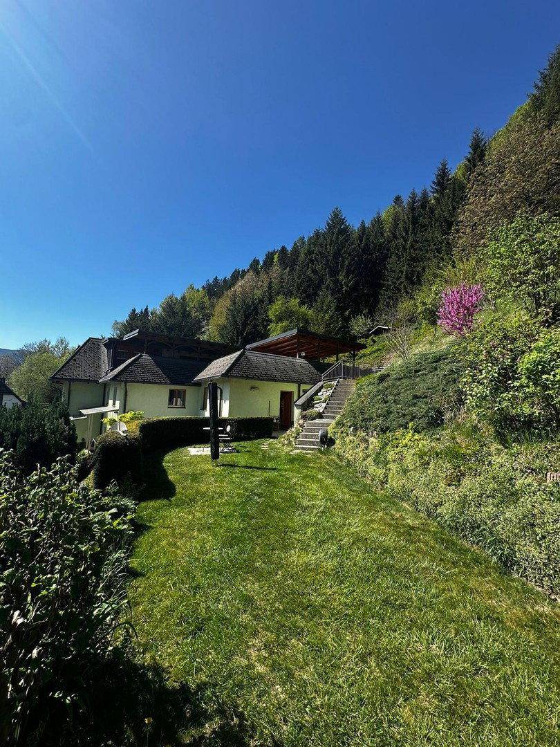 Hausansicht vom weitläufigen Garten aus mit Treppenaufgang und umgebender Natur.