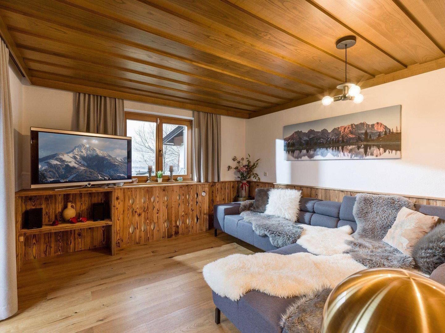 Wohnzimmer im alpinen Stil mit Holzwänden, bequemer Sitzecke und Fernseher.