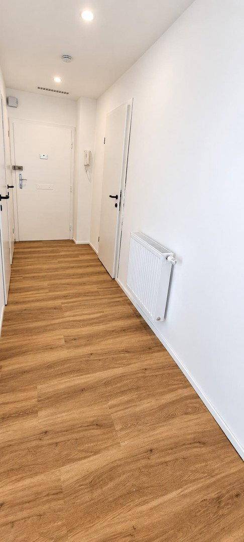Heller Eingangsbereich mit Laminatboden und weiß gestrichenen Wänden, der zu den Wohnräumen führt.