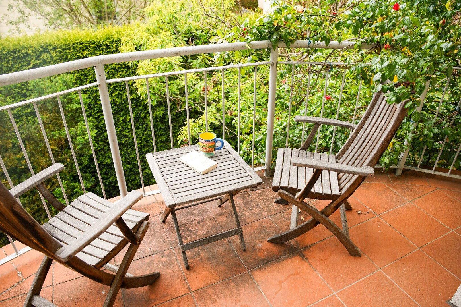 Gemütlicher Balkon mit Holztisch und Stühlen, umgeben von üppigem Grün.