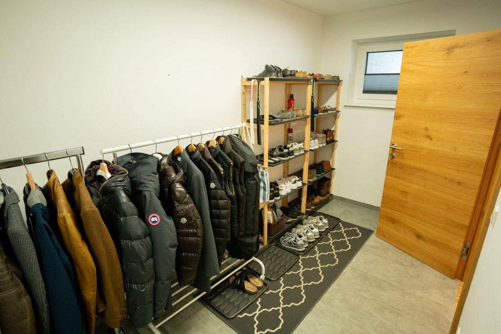 Heller Eingangsbereich mit offener Garderobe, Schuhregalen und Holztür.