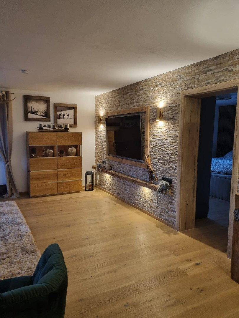 Wohnzimmer mit Steinwand, integriertem Fernseher und indirekter Beleuchtung, Holzboden.