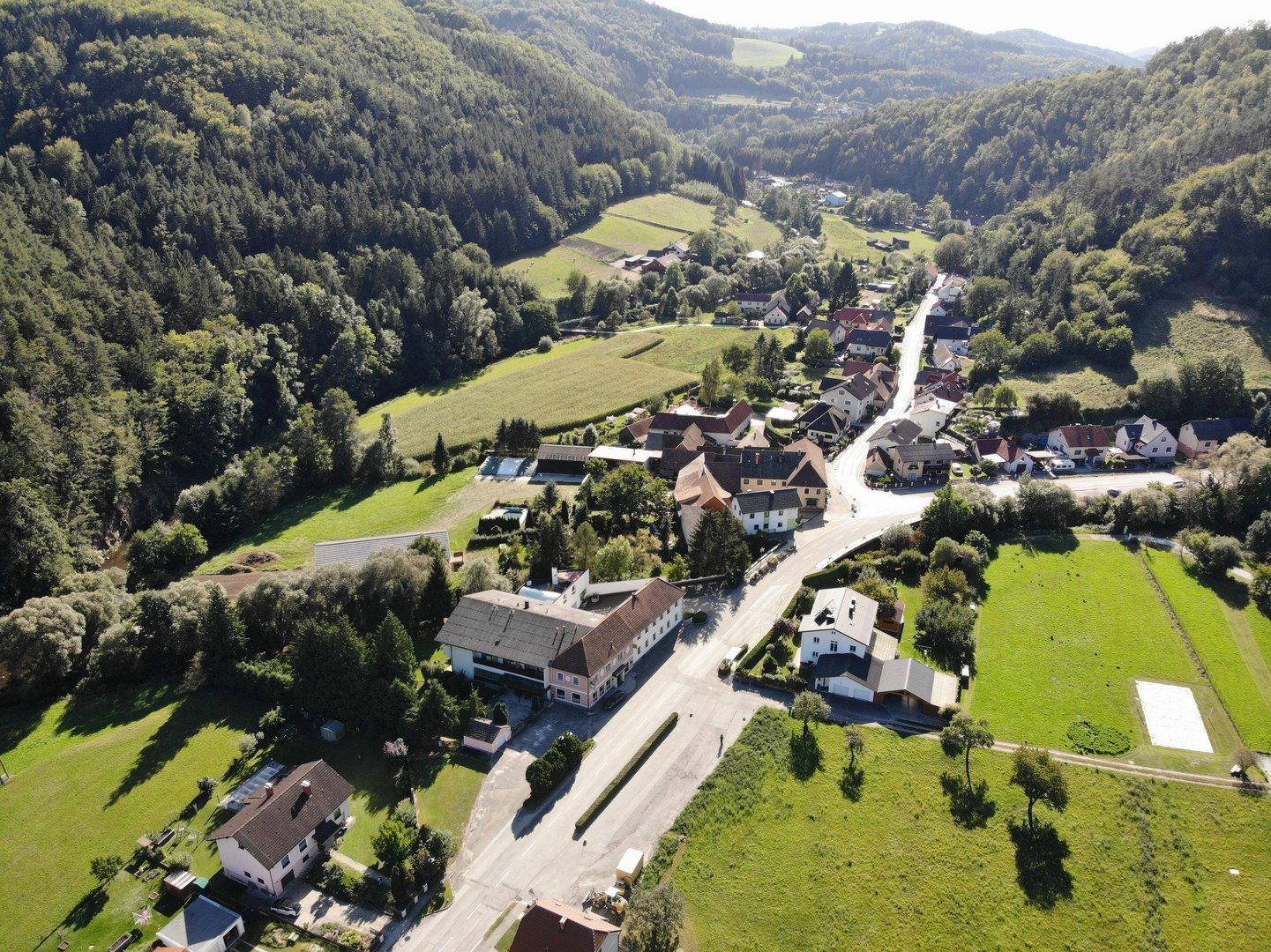Weitläufige Luftaufnahme eines malerischen Dorfes eingebettet in eine grüne Hügellandschaft.